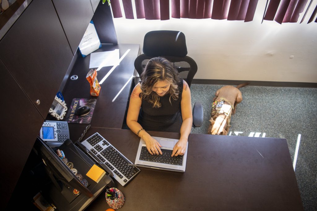 Jen Wong, 374th Airmen Family Readiness Center director, works at her desk while her dog Casey sits along side her. Casey accompanies Wong to work almost everyday to provide Jen support she needs while also bringing joy to Yokota Airmen. (U.S. Air Force photo by Staff Sgt. Ryann Holzapfel)